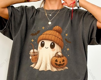 Può includere: T-shirt grigio scuro con un fantasma dei cartoni animati che indossa un berretto marrone, tiene in mano una zucca e un caffè. Il fantasma sorride, con pipistrelli e stelle intorno. Il testo "The GoodKitty Designs" è visibile.