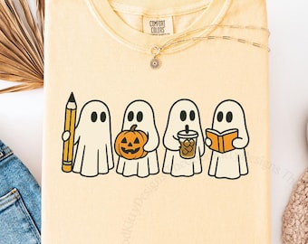 May include: Butter-colored t-shirt featuring a line of four cartoon ghosts, each holding a different item: a pencil, a jack-o'-lantern, a coffee cup, and a book. The shirt is paired with blue jeans and white slip-on shoes.