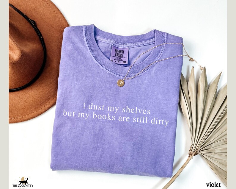 May include: A lavender colored t-shirt with the text "i dust my shelves but my books are still dirty" printed in white.
