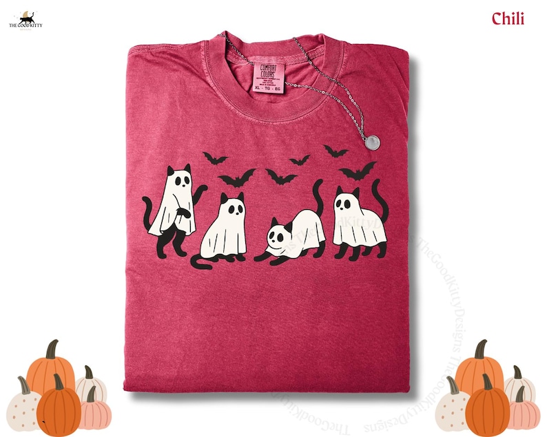 May include: A red t-shirt featuring a Halloween design with four cats dressed as ghosts and black bats. The shirt has a crew neck and short sleeves. The text "Chili" is visible in the upper right corner.
