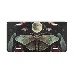 May include: A dark green moth with a large wingspan flies in front of a full moon. The moth is surrounded by small pink and purple butterflies, green leaves, and red flowers. The background is a dark blue night sky with stars.