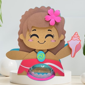 Puede incluir: Un personaje de dibujos animados de pelo castaño con una flor rosa en el pelo, que lleva un collar de flores rojo y azul y sostiene una concha rosa. El personaje está hecho de cartón y está de pie sobre una plataforma blanca.