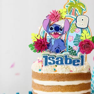 Puede incluir: Una tarta de capas coronada con un adorno colorido que presenta al personaje Stitch, una tabla de surf y flores tropicales. El adorno también incluye el nombre "Isabel" y el número "9". Un gorro de fiesta es visible en el fondo.