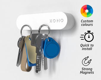 May include: White magnetic key holder with the word "OHOH" printed on it. The key holder has a row of keys attached to it. The image also includes three icons: a color wheel, a stopwatch, and a magnet.