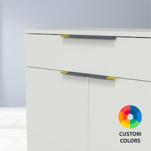 May include: White cabinet with two drawers and a door, featuring dark gray and gold-toned hardware. The cabinet has a clean, modern design. The image includes a color wheel with the text "CUSTOM COLORS".