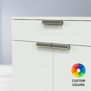 May include: White cabinet with two gray and yellow cabinet pulls. The pulls are rectangular with rounded ends and a yellow border. The cabinet has a clean, modern design. The text "CUSTOM COLORS" is in the lower right corner.