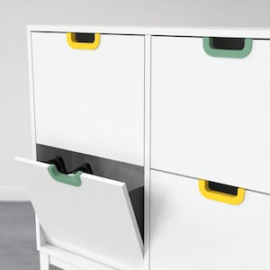 Puede incluir: Gabinete blanco con cuatro cajones, cada uno con un tirador de color. Un cajón está abierto, revelando un objeto negro en el interior. Los tiradores son amarillos y verdes.