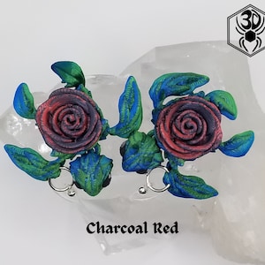 May include: A pair of earrings featuring a rose design with charcoal red and blue accents. The earrings are made of polymer clay and have a textured finish.