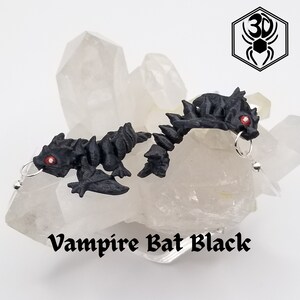 K&ouml;nnte beinhalten: Ein Paar schwarze Fledermaus-Ohrringe mit roten Augen. Die Ohrringe sind aus Polymer Clay gefertigt und h&auml;ngen an silbernen Haken.