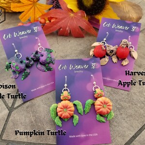 K&ouml;nnte beinhalten: Vier Paar handgefertigte Ohrringe aus Polymer Clay mit einem Schildkr&ouml;ten-Design. Die Ohrringe sind in vier verschiedenen Stilen erh&auml;ltlich: Poison Apple Turtle, Harvest Apple Turtle, Pumpkin Turtle und eine gr&uuml;ne und violette Schildkr&ouml;te. Jedes Paar Ohrringe ist mit dem Namen des Stils und dem Markennamen "Crb Weaver 3D Jewelry" gekennzeichnet.