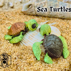 May include: Two 3D-printed sea turtle figurines with brown and black shells and green flippers and heads. The turtles are on a bed of sand with a seashell. The text "Sea Turtles" is above the turtles.