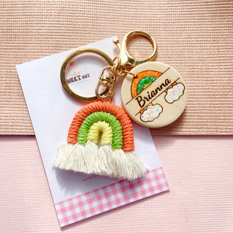 May include: A rainbow-colored keychain with a wooden charm that says "Brianna" with a rainbow and clouds. The keychain is made of yarn and has white tassels.