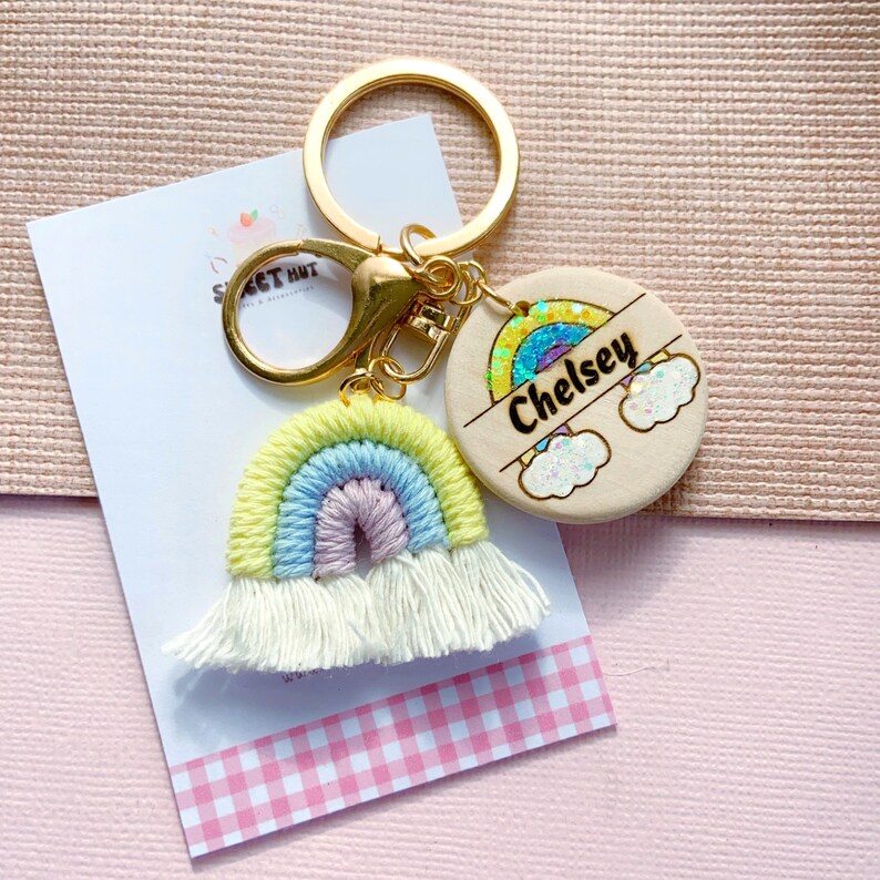 May include: A rainbow-colored crocheted keychain with a white tassel, attached to a gold key ring and a round wooden tag with the name "Chelsey" and a glittery rainbow design.