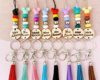 May include: Set of ten personalized keychains with wooden tags, colorful beads, and tassels. The tags feature names like "Mrs. Adams", "Miss Wood", and "Miss Sanchez".