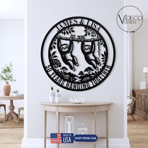 May include: Black metal wall art featuring two sloths hanging from a branch, with the names "JAMES & LISA" and "EST. 1976" above. The text "50 YEARS HANGING TOGETHER" is below. The design is circular and decorative.