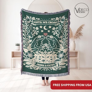 May include: A dark green woven throw blanket featuring a cream-colored illustration of two frogs holding hands under a crescent moon and stars. The text reads UNTIL WE CROAK and JAMES & KATHY. The blanket has a fringed edge and floral motifs.