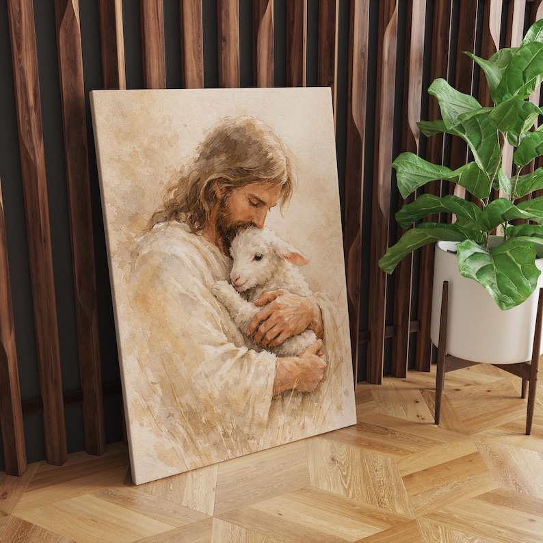 May include: A framed canvas print depicts a tender scene of a figure with long hair and a beard cradling a lamb. The artwork is rendered in soft, warm tones, with the figures in white robes. The background is a muted, neutral color.