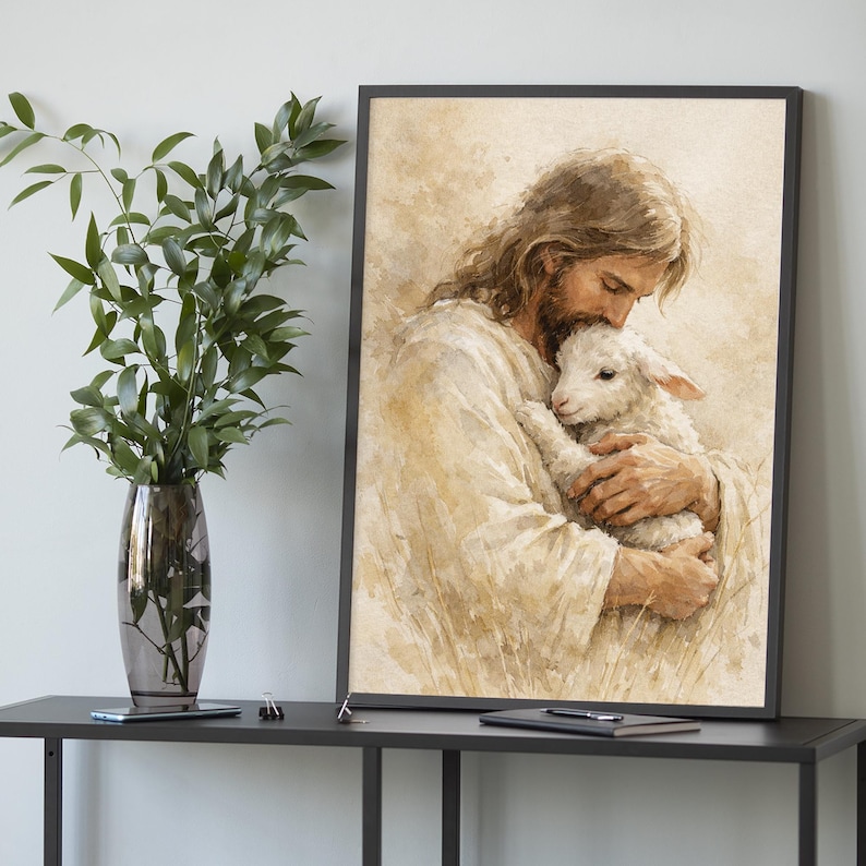 May include: A framed watercolor print depicts a figure with long brown hair and a beard, dressed in white robes, cradling a white lamb. The artwork has a soft, warm color palette and is set against a neutral background.