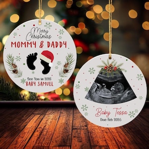 May include: Two round Christmas ornaments with gold string. One ornament has the text "Merry Christmas MOMMY & DADDY" and "See You in 2026 BABY SAMUEL". The other ornament has a baby ultrasound image and the text "Baby Tessa Due Feb 2026".