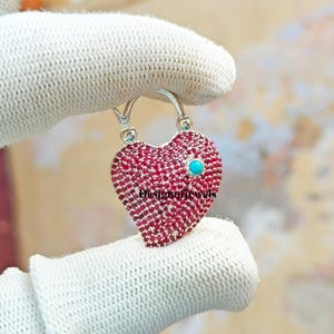 May include: A silver heart-shaped padlock pendant with a turquoise stone in the center. The padlock is covered in small red gemstones.