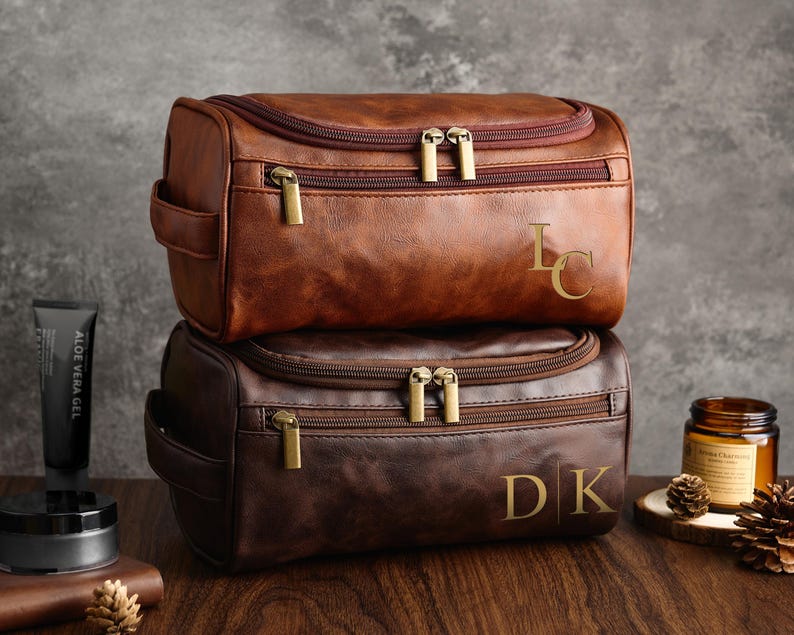 May include: Two brown leather travel bags with zipper closures and gold hardware. The top bag has the initials "LC" embossed on the front. The bottom bag has the initials "DK" embossed on the front.