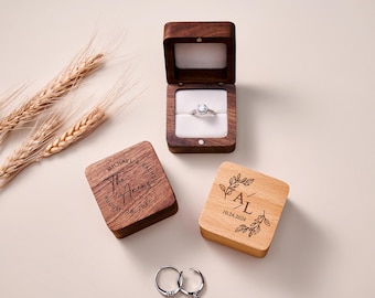 May include: An open wooden ring box with a diamond engagement ring, next to two closed wooden ring boxes. One box is engraved with a couple's names and a date. The other box is engraved with initials and a date. Two rings are at the bottom.