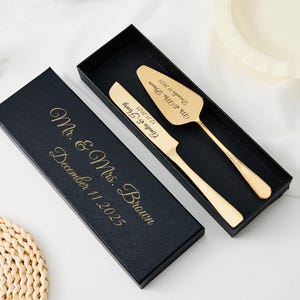 Può includere: Un set di coltello e paletta per torte color oro in una scatola nera. Il coltello e la paletta sono incisi con nomi e una data. La scatola è anche iscritta con le parole "Mr. & Mrs. Brown" e la data "11 dicembre 2025".