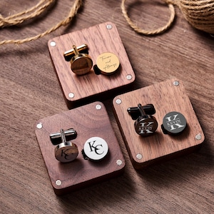 May include: Three sets of personalised cufflinks and matching round accents on wooden display blocks. One set is gold-toned with the inscription "Forever and Always." Another set features the initials "KC," and the third set has the name "KEVIN."