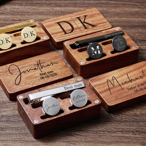 May include: Set of six wooden boxes with engraved names and dates. Each box contains a tie clip and cufflinks. The boxes are made of dark wood with a natural finish.