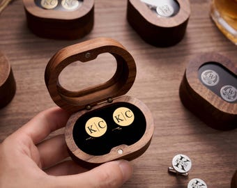 May include: A wooden oval box with a clear top, open to reveal two gold cufflinks with the initials "KC". Several other wooden boxes with cufflinks are visible on a wooden surface. The cufflinks are a personalized gift.