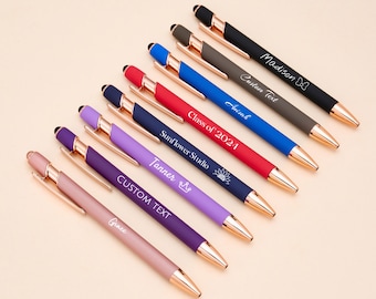 May include: A set of ten personalized pens with rose gold accents. The pens are in various colors, including purple, pink, blue, red, and black. Each pen has a different name or message engraved on it, such as "Grace", "Tanner", "Custom Text", "Sunflower Studio", "Class of 2021", "Isaiah", "Custom Text", and "Madison".