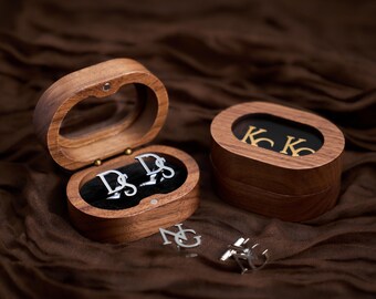 May include: Wooden oval boxes with personalized cufflinks. One box is open, revealing silver cufflinks with the initials "DS". Another box displays gold cufflinks with the initials "KK". Additional cufflinks with the initials "NG" are also visible.