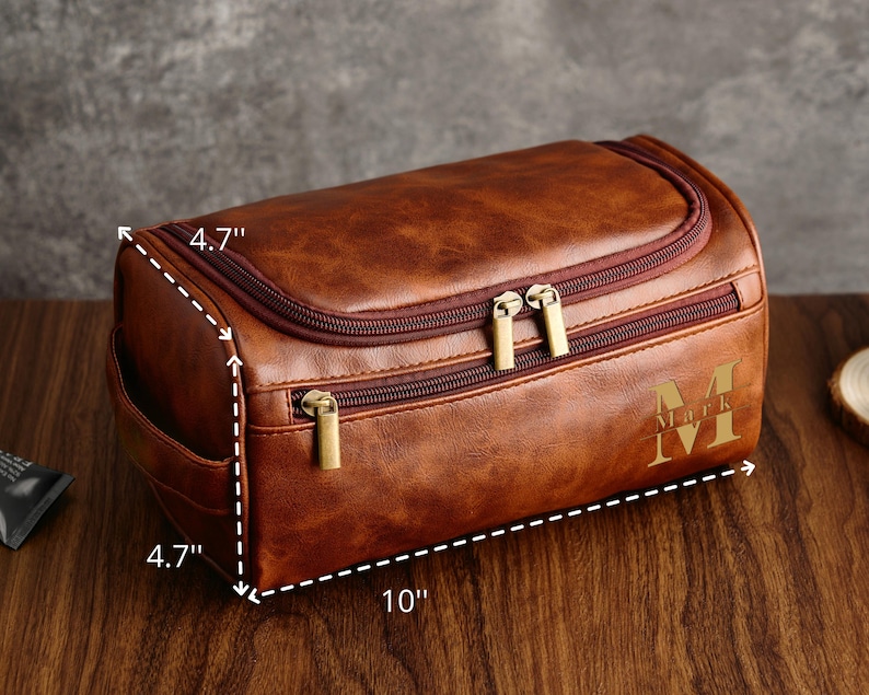 May include: A brown leather travel toiletry bag with two zippers and a gold zipper pull. The bag measures 10 inches long, 4.7 inches wide, and 4.7 inches high. The bag has a monogrammed initial "M" on the front.