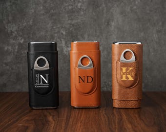 May include: Three leather cigar cases in black, tan, and brown, each with a silver cigar cutter. The black case has the initial "N" and the text "Nathan Groomsmen". The tan case has the initials "ND", and the brown case has the initial "K" and the name "Kevin".