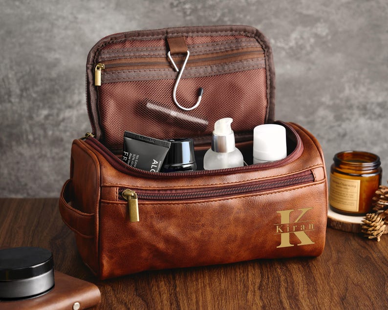 May include: Brown leather travel toiletry bag with a zipper closure and a gold monogram that says "Kiran".