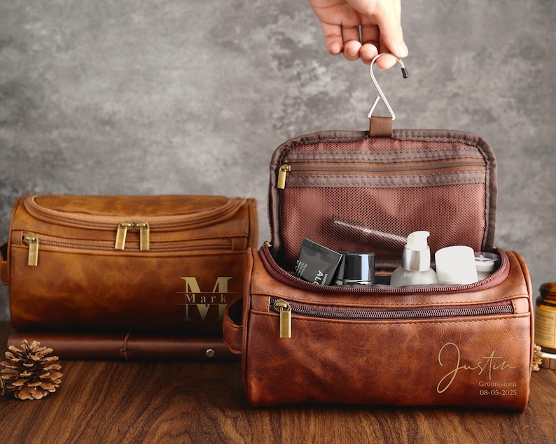 May include: Two brown leather travel bags with zipper closures. The bag on the left has the name "Mark" embossed on the front. The bag on the right is open and has a mesh pocket inside. The bag on the right has the name "Justin" and the date "08-05-2023" embossed on the front.