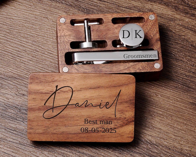 May include: A wooden box with a personalised inscription reading "Daniel Best man 08-05-2025". The box contains a tie clip engraved with "Groomsmen" and a cufflink set with the initials "D|K".