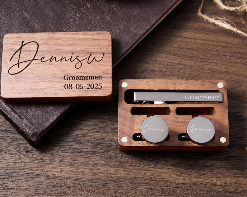 May include: Wooden box containing a tie clip and cufflinks. The box is engraved with the name "Dennis" and the text "Groomsmen 08-05-2025".