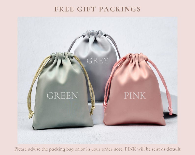 May include: Three satin drawstring pouches in green, grey, and pink. Each pouch features a matching drawstring closure and the color name printed in white text on the front. The green pouch has gold cords, while the grey and pink pouches have matching cords.