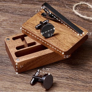 May include: Wooden box with three compartments for storing cufflinks and a tie clip. The box is 1 inch tall, 2.6 inches wide, and 0.75 inches deep. The tie clip is 2.1 inches long and 0.3 inches wide. The cufflinks are 0.7 inches in diameter.
