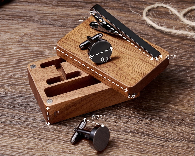 May include: Wooden box with three compartments for storing cufflinks and a tie clip. The box is 1 inch tall, 2.6 inches wide, and 0.75 inches deep. The tie clip is 2.1 inches long and 0.3 inches wide. The cufflinks are 0.7 inches in diameter.