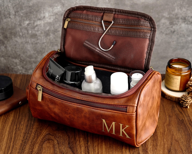 May include: Brown leather travel toiletry bag with a zipper closure and a hook inside. The bag is open and filled with toiletries, including a bottle of lotion, a tube of toothpaste, and a small bottle of shampoo. The bag has the initials "MK" embossed on the front.