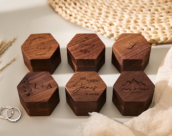 Peut inclure: Six boîtes à bagues hexagonales en bois avec des noms et des dates gravés. Les boîtes sont brun foncé avec un grain de bois naturel. Certaines boîtes portent des noms tels que "Mr. & Mrs. James".