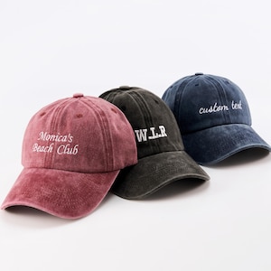 Op de afbeelding: Drie baseballpetten in bordeauxrood, zwart en marineblauw, elk met een gebogen klep en verstelbare band. De bordeauxrode pet heeft de witte tekst "Monica's Beach Club". De zwarte pet heeft de witte tekst "W.L.R". De marineblauwe pet heeft de witte tekst "custom text".