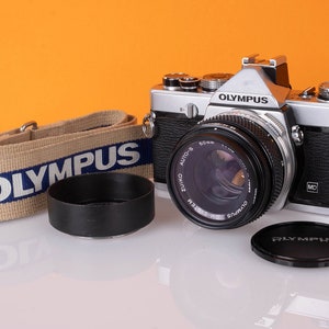 Olympus OM1 film camera with 50mm 1.8 lens, metal lens hood, front lens cap and original Olympus strap