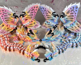 May include: Two colorful, detailed, 3D printed dragon figurines with butterfly wings. The dragons are facing each other and have a segmented, scaly body. The wings are translucent and have a gradient of pink, yellow, and blue.