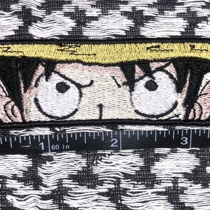 May include: Embroidered patch featuring a close-up of a cartoon character's face with a straw hat. The character has black hair, large eyes, and a serious expression. The patch is approximately 2 inches wide.