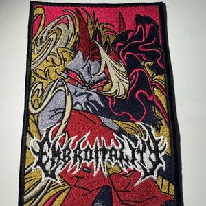 May include: Embroidered patch with a red, black, and white design of a demon with wings. The text "EMBROILMENT" is in white with black outlines.