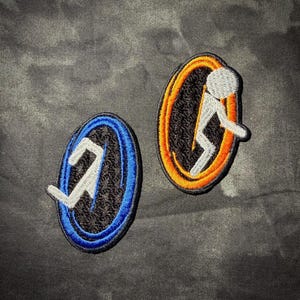 May include: Two embroidered patches featuring oval shapes with black centers. One patch has a bright blue border and the other has a vibrant orange border. Each patch displays a white, stylized figure of a person jumping through the center.