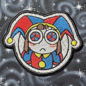 May include: Embroidered patch featuring a cartoon jester with a sad expression. The jester wears a red, blue, and yellow outfit with a matching hat. The jester's eyes have a colorful pinwheel design. The patch has a white border and is on a dark background.
